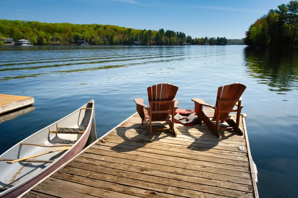 Two Adirondack chairs on a wooden dock facing the blue water of a lake in British Columbia, Canada