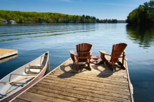 Two Adirondack chairs on a wooden dock facing the blue water of a lake in British Columbia, Canada